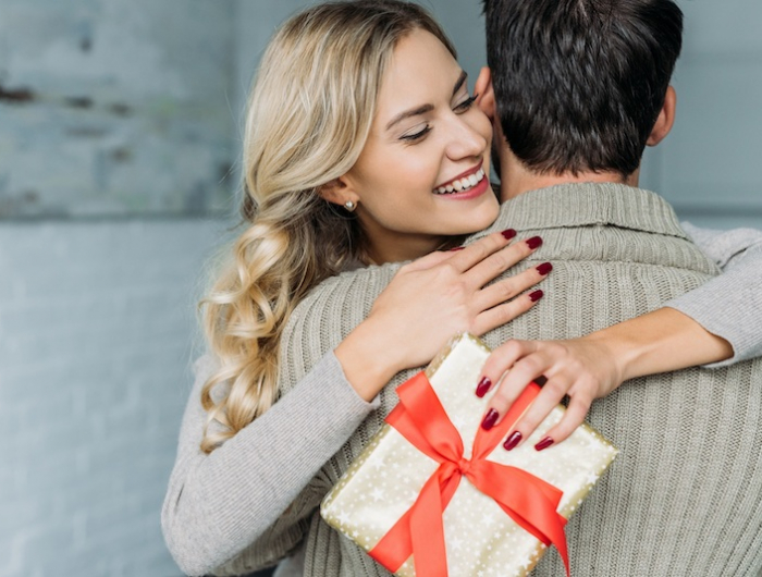 attractive young woman with gift box embracing her boyfriend at home