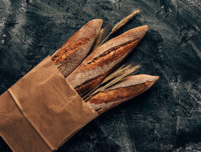 arranged french baguettes in paper bag and wheat on dark tabletop with flour