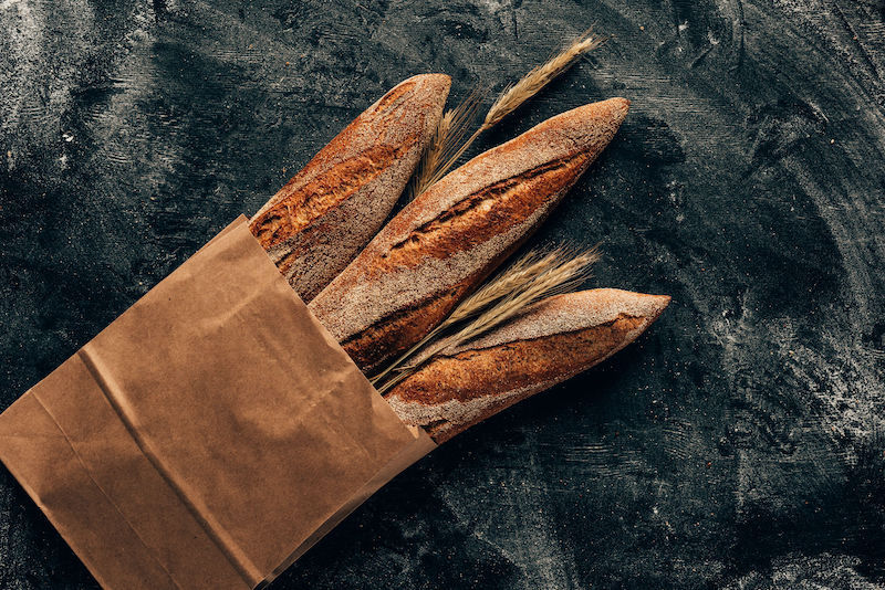 arranged french baguettes in paper bag and wheat on dark tabletop with flour