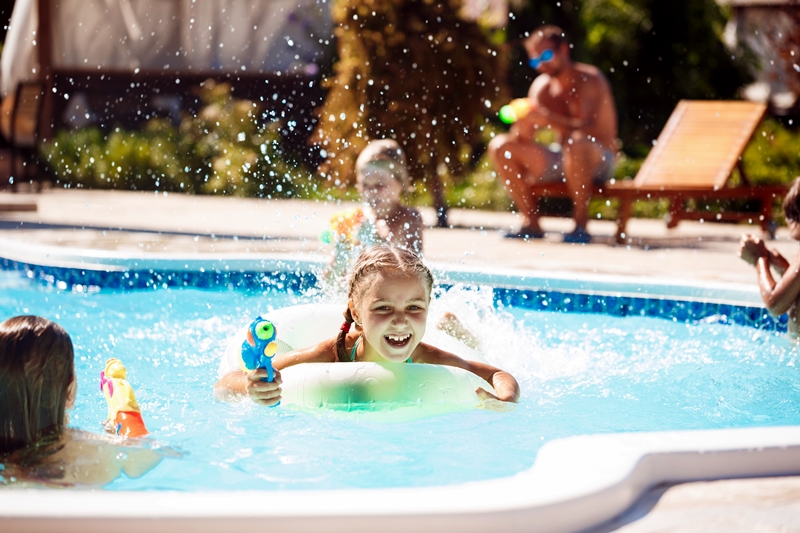 cheerful children playing waterguns, rejoicing, jumping, swimming in pool.