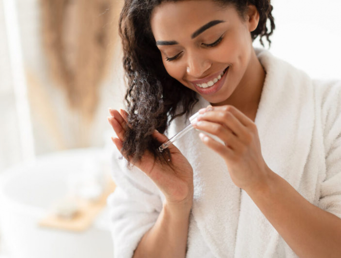 african american woman applying serum on damaged hair in bathroom