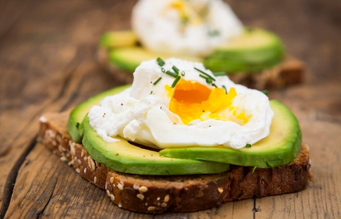 wholemeal bread slices with sliced avocado and poached eggs on wood