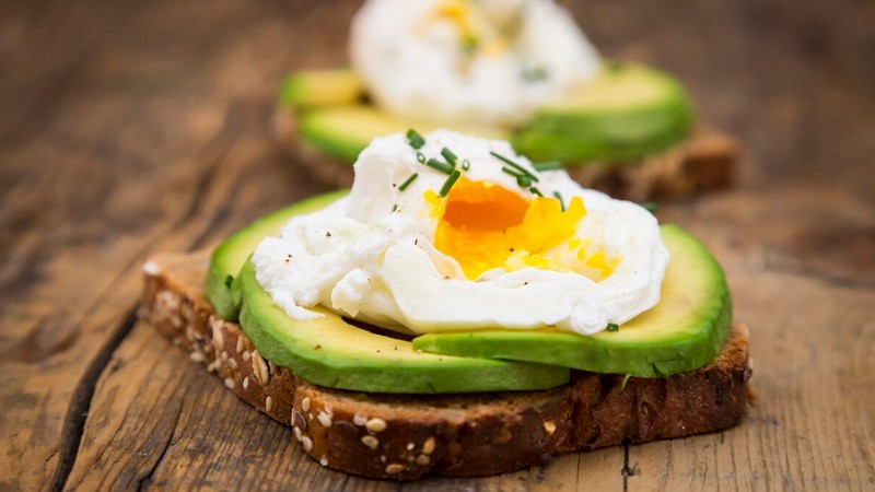 wholemeal bread slices with sliced avocado and poached eggs on wood