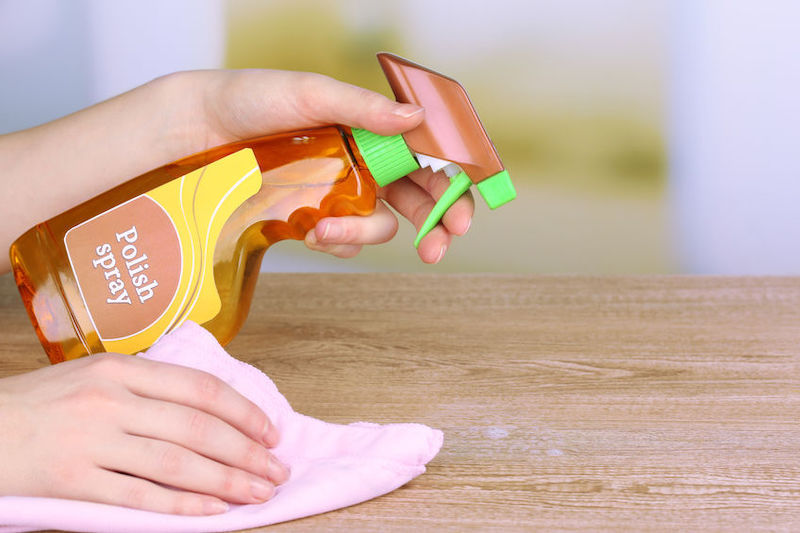hand cleaning wooden table with furniture polish