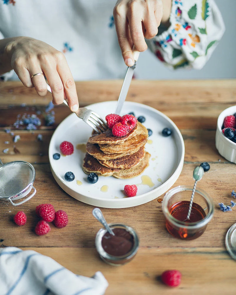 frau isst pancakes mit himbeeren und heidelbeeren