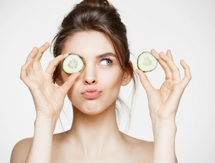 young beautiful naked girl smiling hiding eye behind cucumber slice over white background. beauty spa and cosmetology concept.