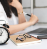 time management, black alarm clock with blurred business woman is working with laptop.