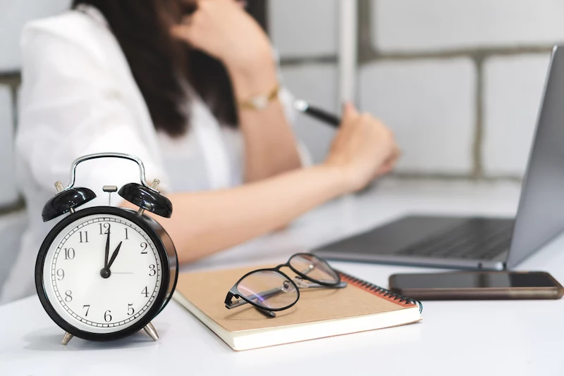 time management, black alarm clock with blurred business woman is working with laptop.