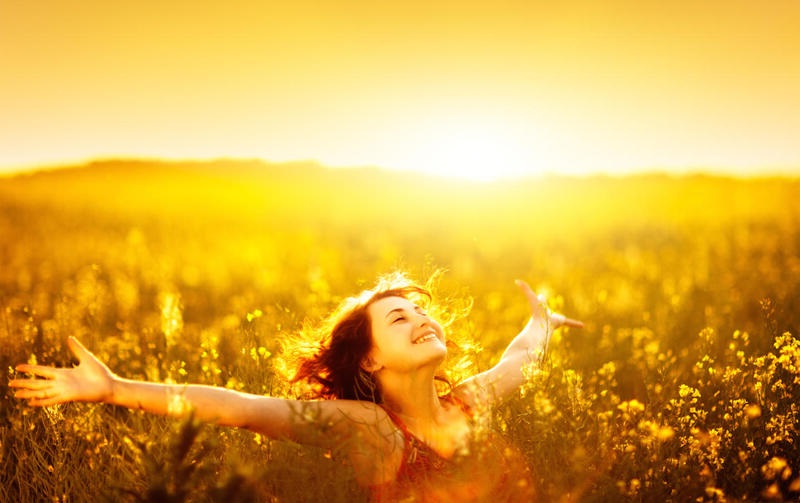 woman in sunny canola field with outstretched arms