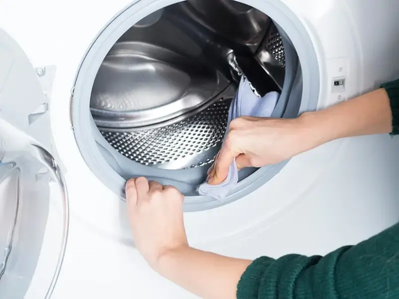 flusensieb der waschmaschine reinigen kommt wasser raus waschmaschine reinigen frau putzt mit tuch die gummi der waschmaschinentuer
