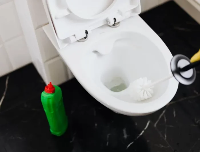person versucht verstopfte toilette mit einer toilettenbürste freizubekommen