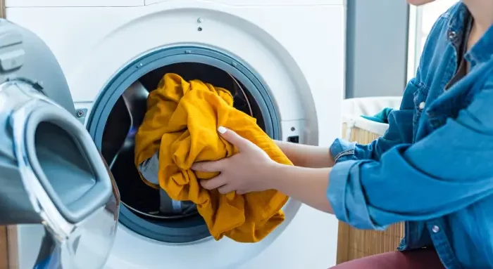 wie oft waschenmaschinenfilter reinigen waschmaschine flusensieb reinigen frau gibt gelbe bluse in die waschmaschine