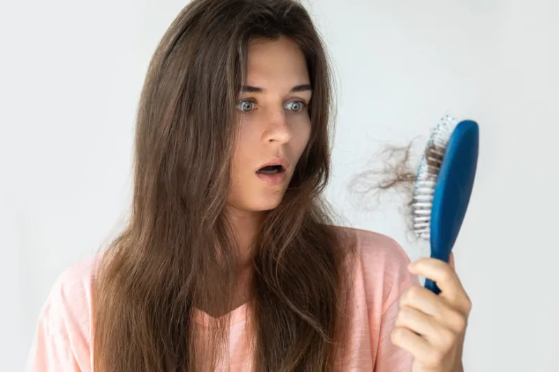 erschrockene frau guckt auf eine haarbuerste voll mit ausgefallenen haaren