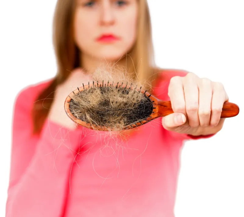 frau zeigt eine buerste mit vielen ausgefallenen haaren haarausfall gruende