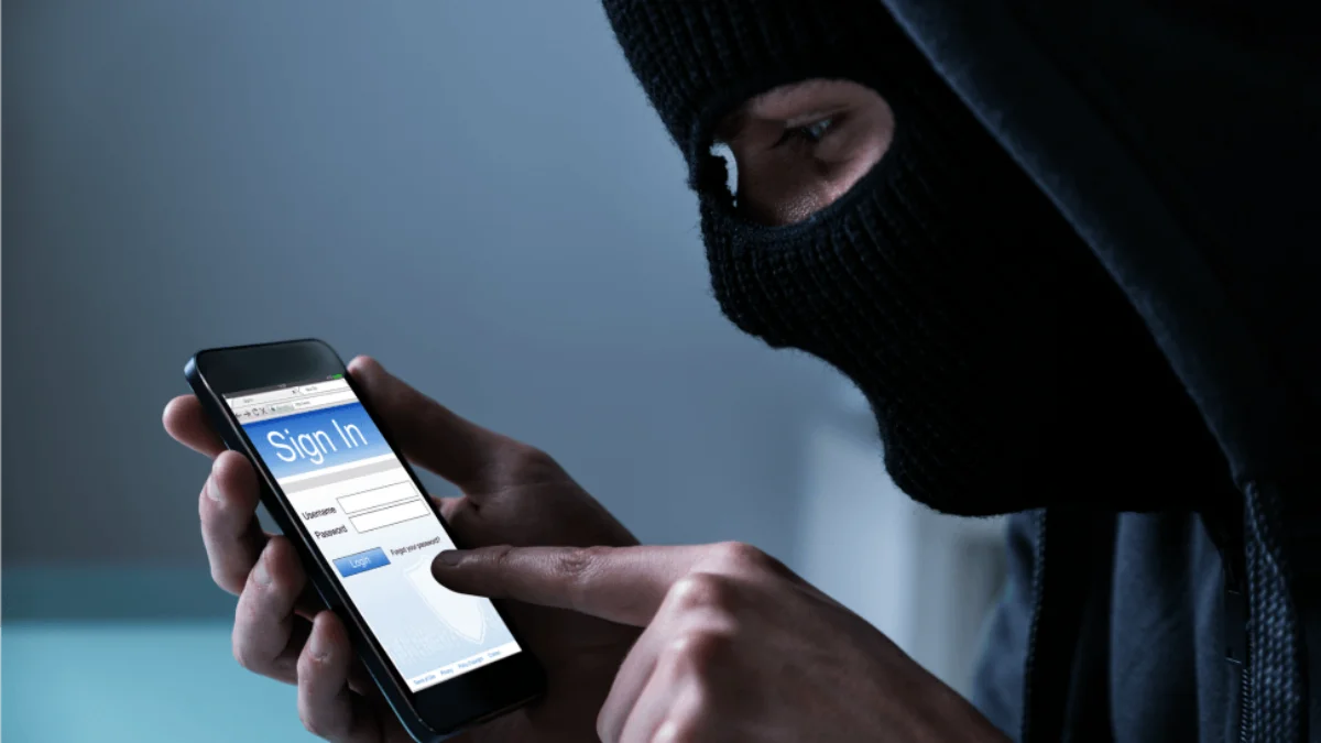 hacker mit schwarzer maske auf dem gesicht beim hacken eines smartphones