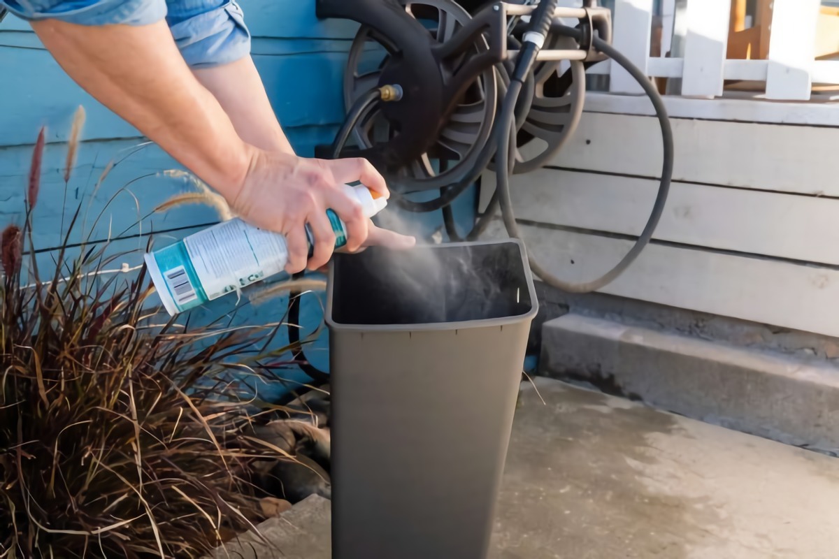 mann im blauen hemd besprueht plastikmuelleimer mit einer flasche desinfektionsmittel