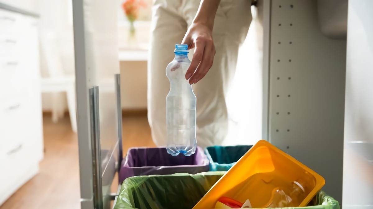 eine frau in weissen hosen wirft eine blaue plastikflasche in einen muelleimer