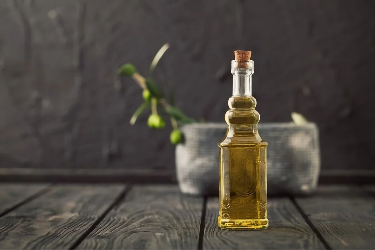 eine glasflasche mit olivenoel steht auf einem holztisch vor einer keramikschale mit einem olivenzweig