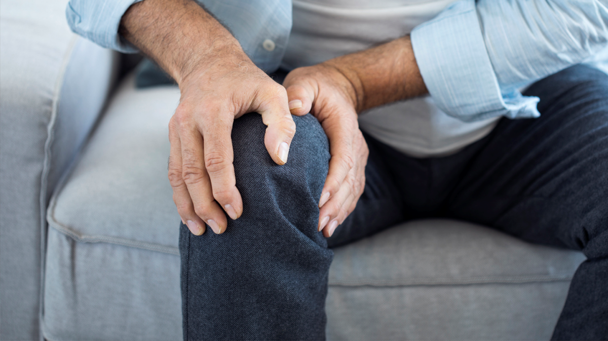 knieschmerzen bei belastung was tun was tun gegen knieschmerzen mann sitzt am sofa haelt sich am knie hat schmerzen