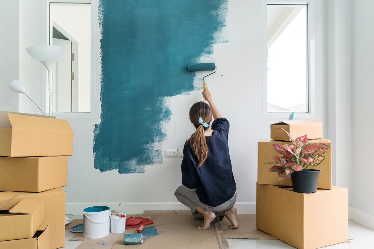 frau mit blauem t shirt und grauer hose streicht wand mit blauer farbe