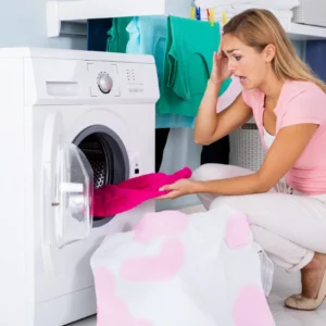 frau mit rosafarbenem t shirt und weissen jeans schaut auf ein beschaedigtes rosa handtuch in der waschmaschine