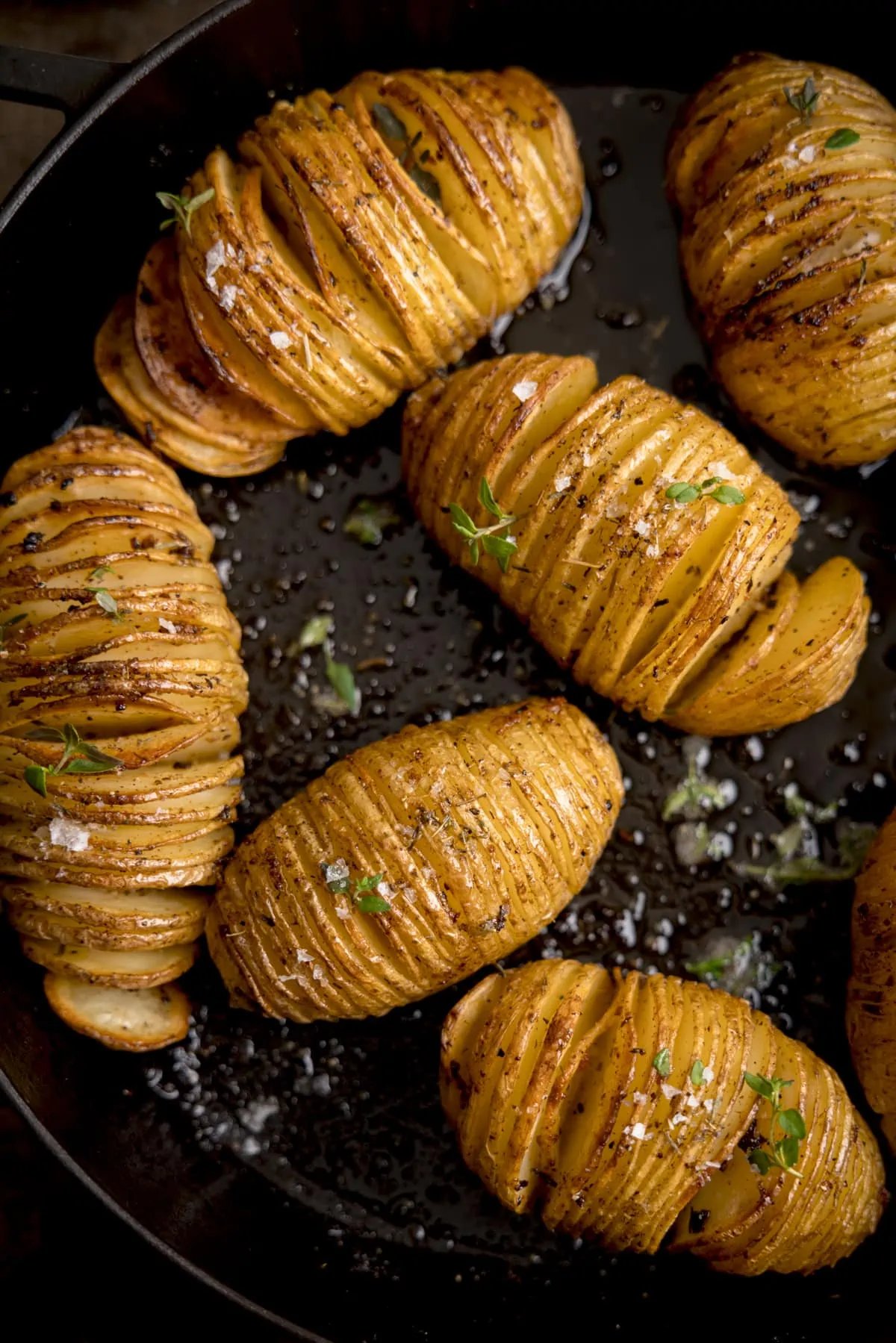 hasselback kartoffeln beim kochen in der schwarzen pfanne mit oel und meersalz