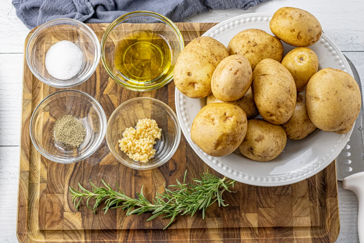 kartoffeln in weissem teller salz oell pfeffer knoblauch und thymian auf holzbrett