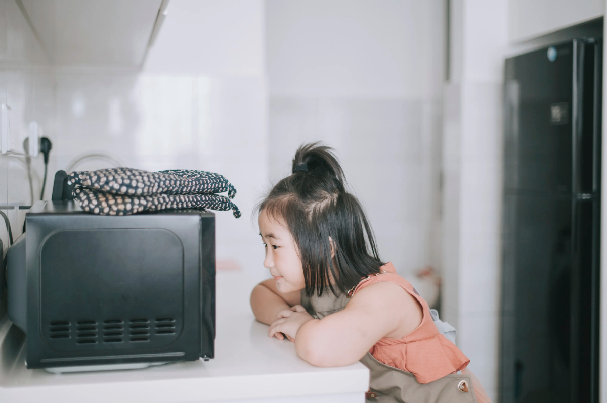 kind mit schwarzen haaren wartet neben der mikrowelle die langsam kocht