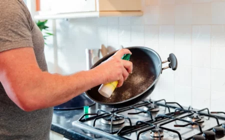 mann mit grauem t shirt besprueht schwarze pfanne vor dem kochen mit kochspray