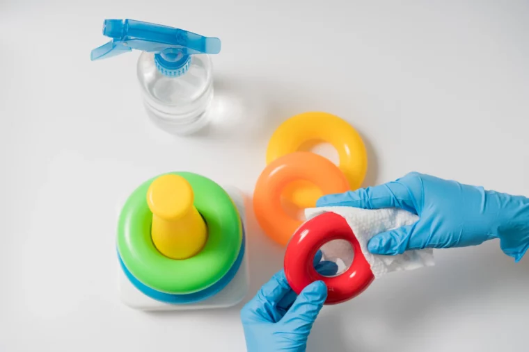 person mit blauen handschuhen die babyspielzeug mit bleichmittel desinfiziert