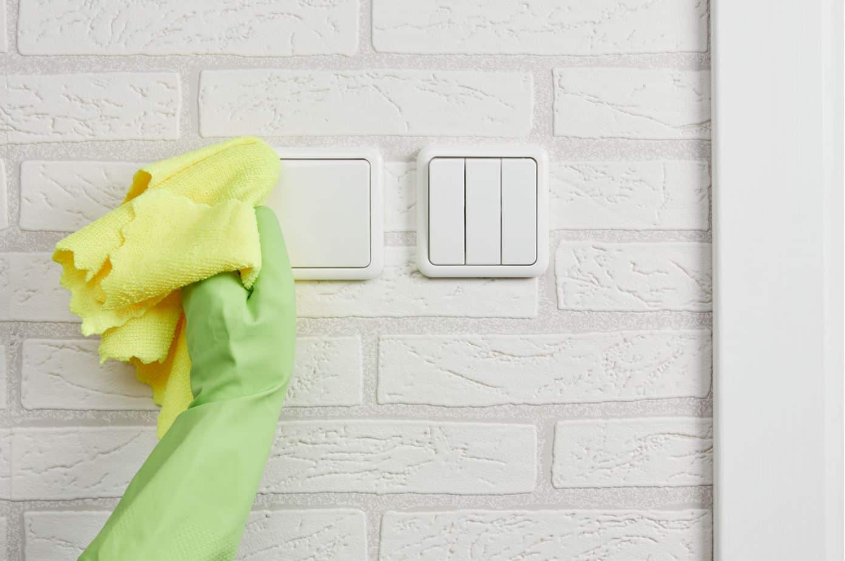 person mit gruenen handschuhen vergilbte lichtschalter mit gelbem handtuch reinigen