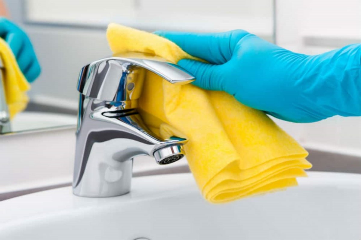 reinigung einer wasserhahngriffe mit gelbem handtuch und blauem handschuh