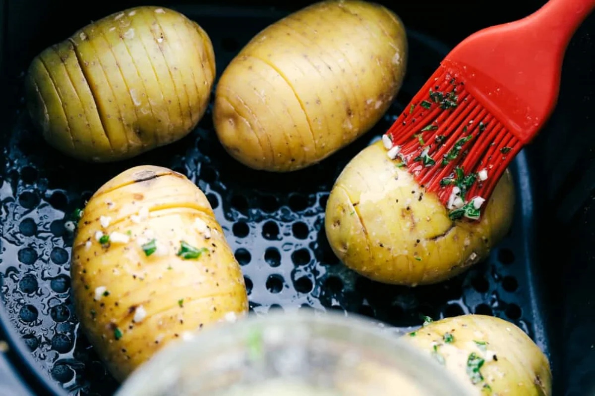 zubereitung von hasselback kartoffeln in einem airfryer und auftragen von butter und kraeutern mit einer roten gummibuerste