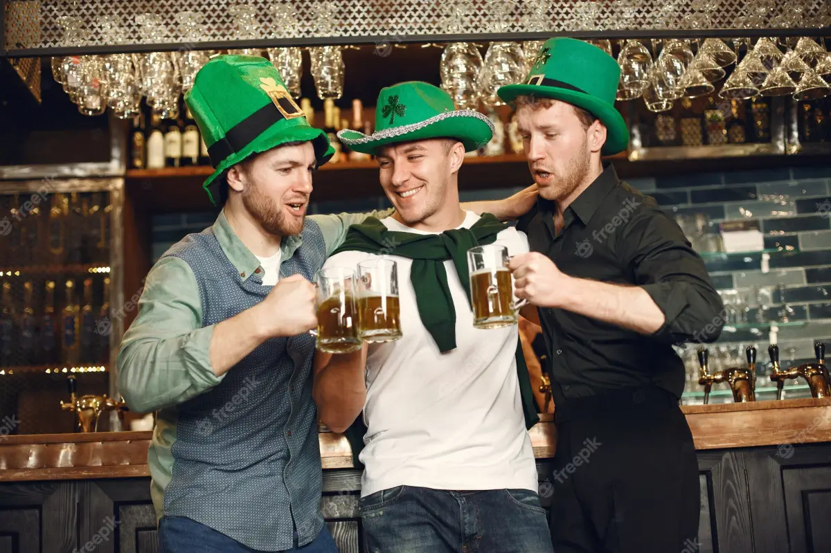 wie wird st patricks day noch genannt drei maenner in kneipe mit gruenen hueter trinken bier