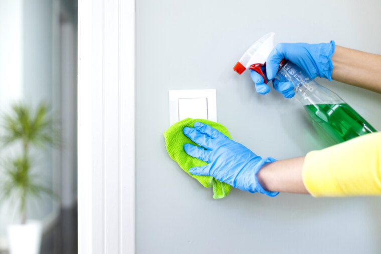 woman cleaning a light switch with a disinfecting spray