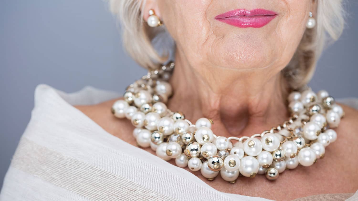 Ältere frau trägt stilvolle halskette mit perlen und weiße bluse und rosa lippenstift