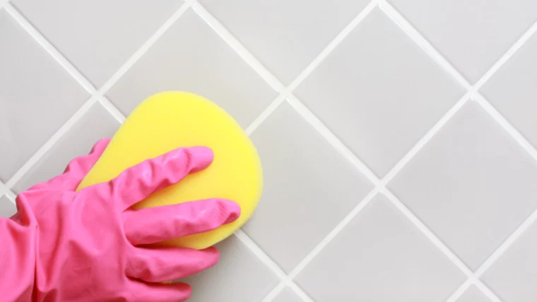 badfliesen mit gelbem schwamm und rosa gummihandschuhen reinigen