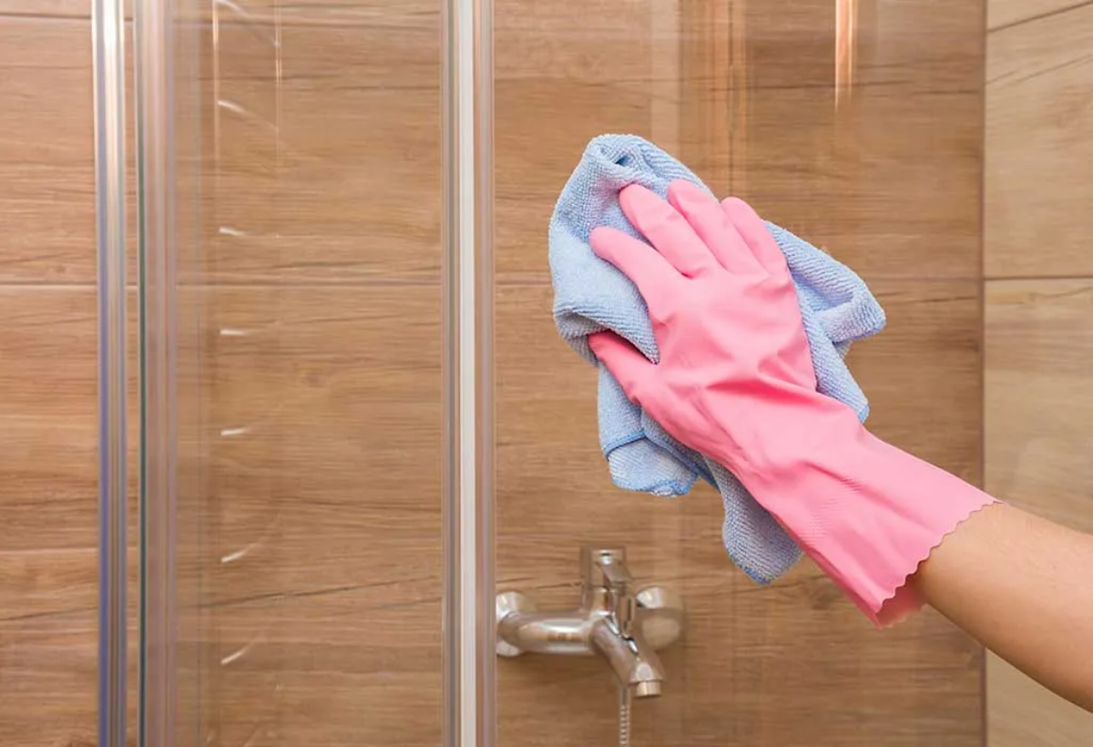 duschtüren im badezimmer mit blauem handtuch und rosa gummihandschuhen reinigen