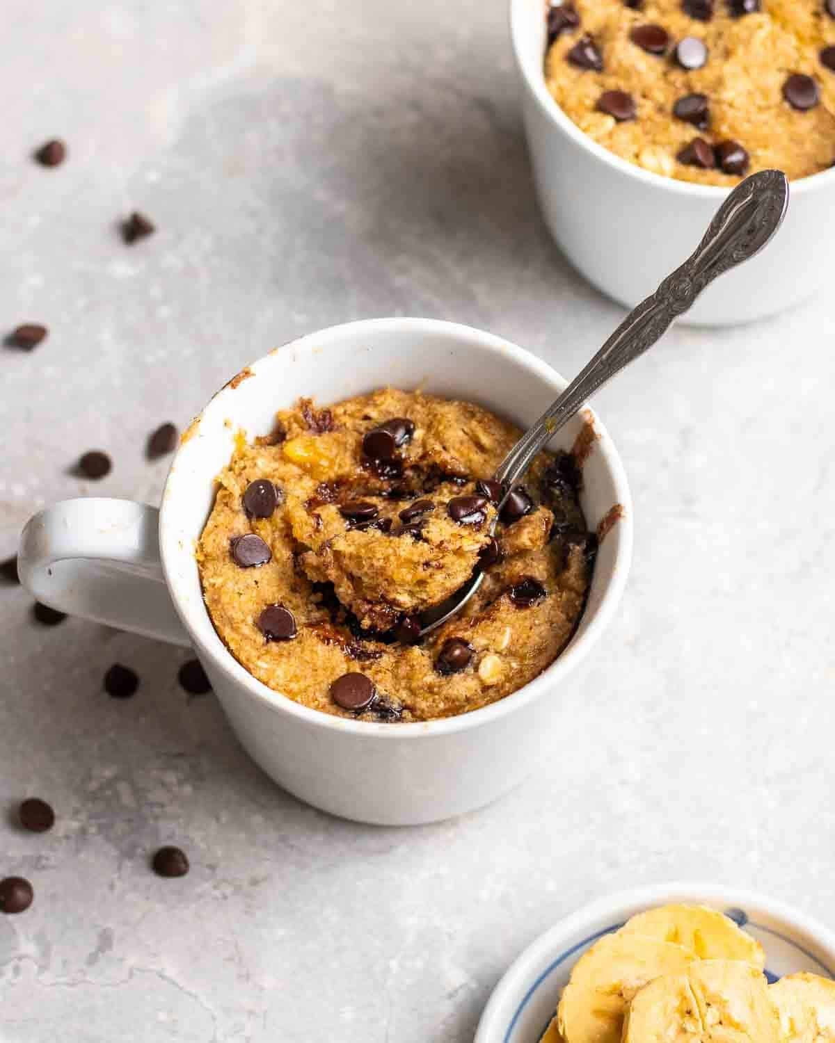 eierloser tassenkuchen in weißer tasse mit haferflocken und schokoladenstückchen mit löffel innen