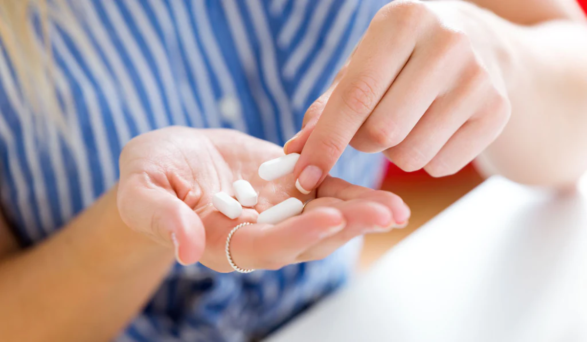 frau mit blauem hemd und silbernem ring nimmt tabletten probiotika als hausmittel gegen blasenentzündung