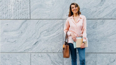 frau über 60 trägt rosa hemd skinny jeans und braune tasche