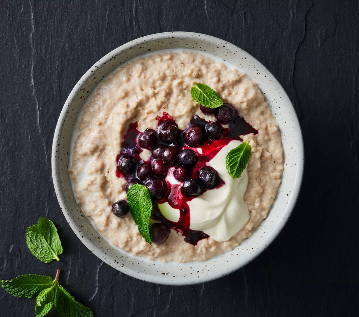 cremiges porridge in weißer schale mit beeren und joghurt und minze
