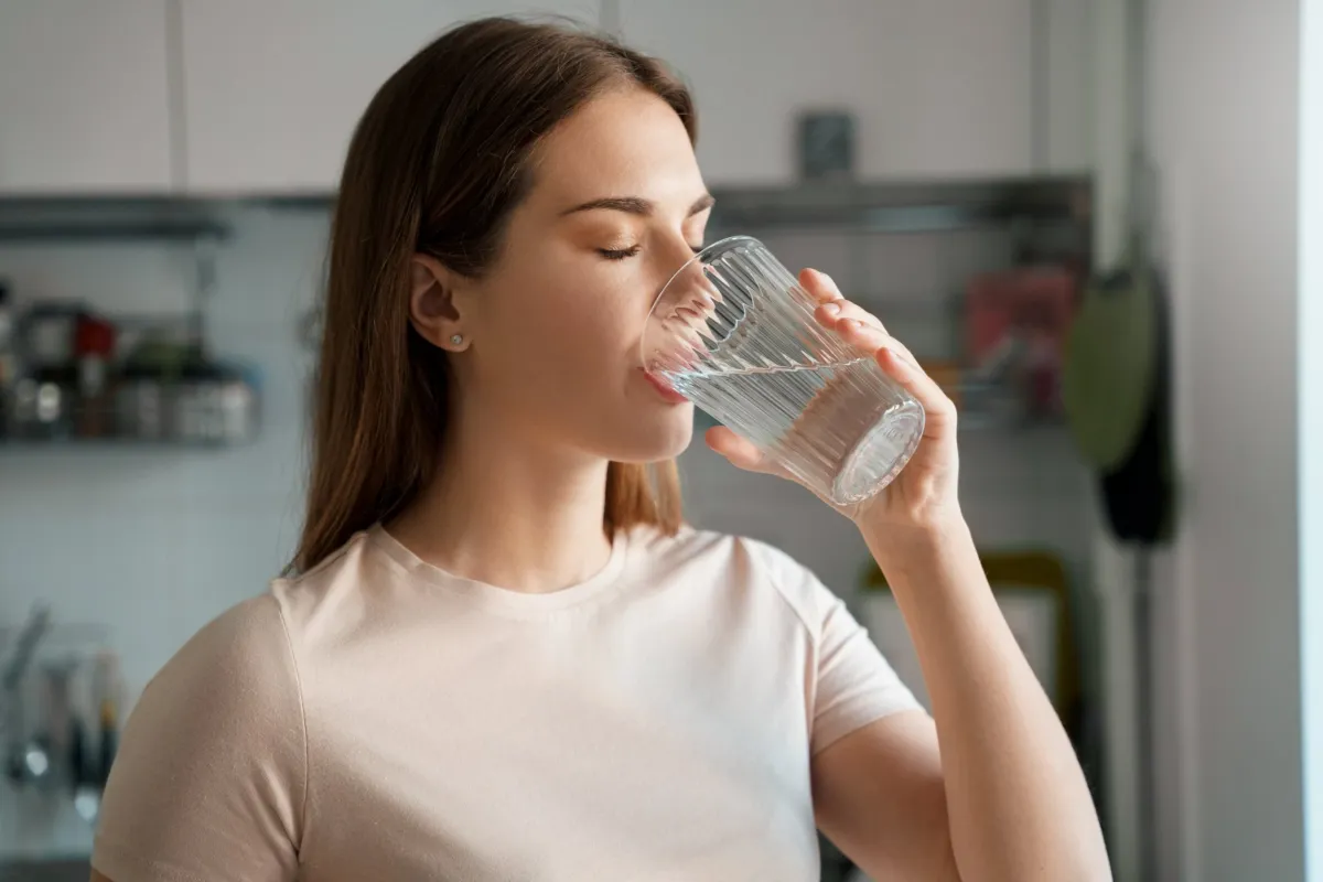 frau schwarze haare weißes shirt trinkt wasser glas