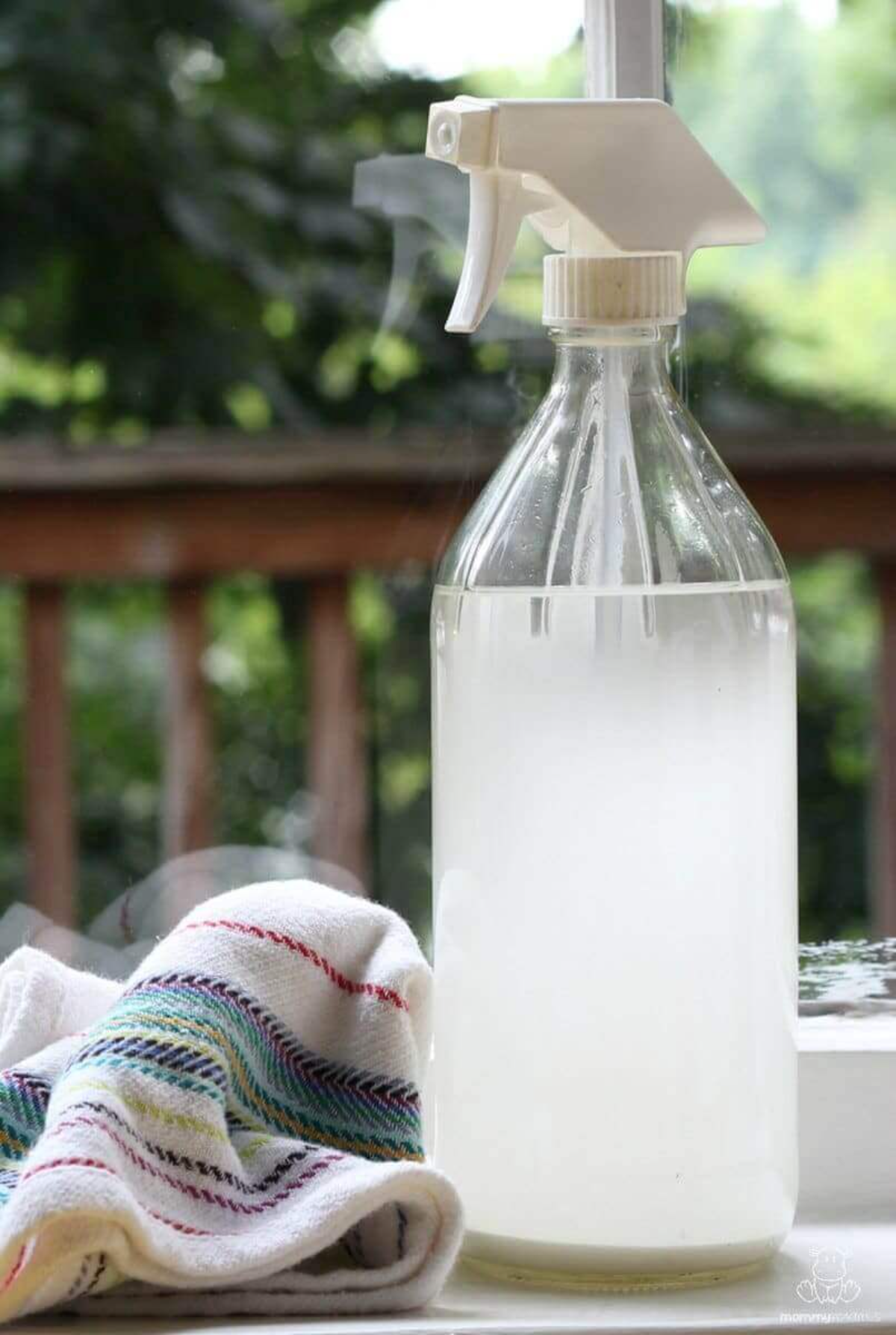 selbstgemachter glasreiniger in weißer flasche neben einem bunten handtuch