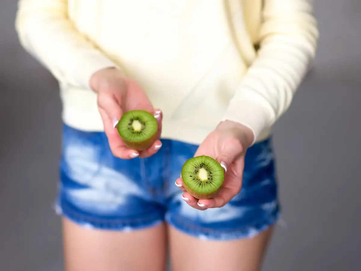 wie isst man kiwibeeren kiwi mit schale essen frau in shorts haelt zwei haelfte von kiwi