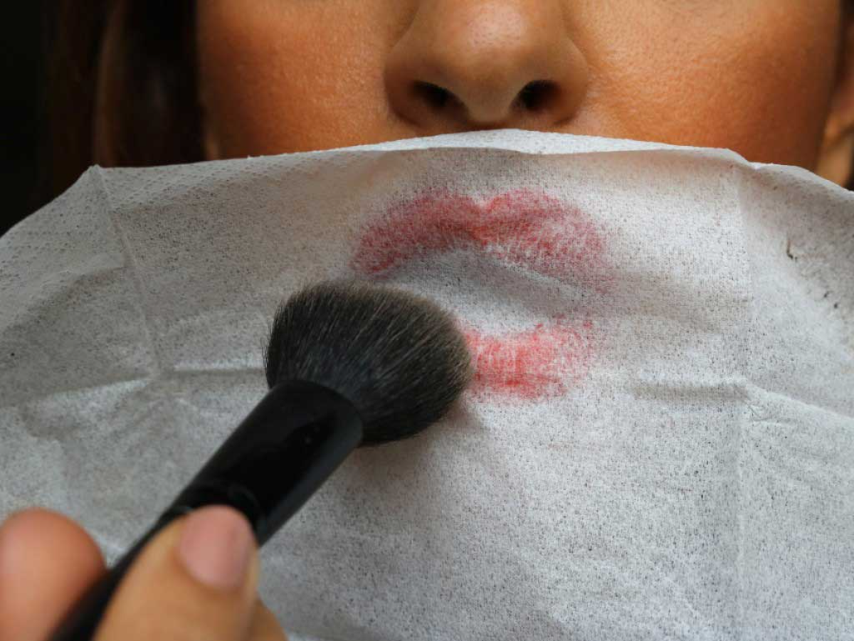 frau mit rotem lippenstift und taschentuch auf den lippen trägt puder auf, um den lippenstift länger haltbar zu machen