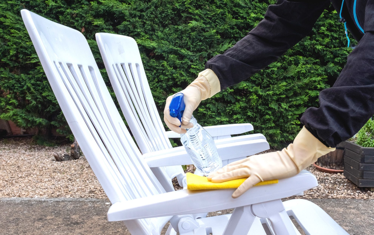 person mit weißen gummihandschuhen reinigt weiße gartenstühle mit gelbem handtuch