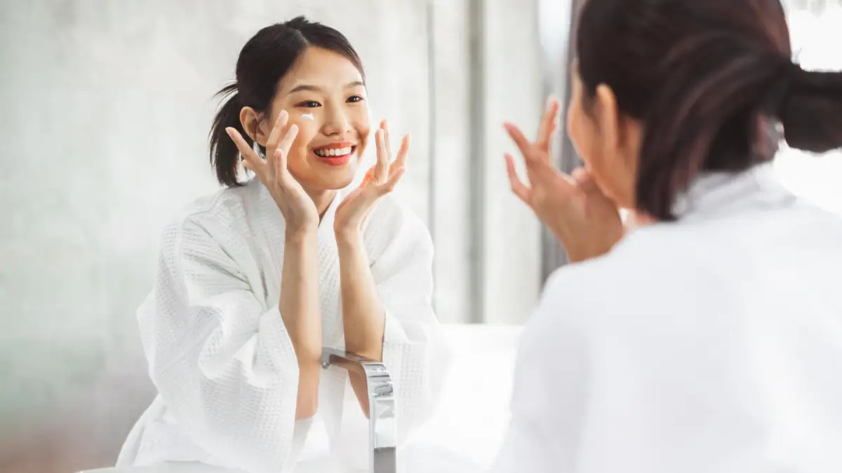 koreanische kosmetik kaufen junge frau schaut sich in den spiegel tupft ihr gesicht