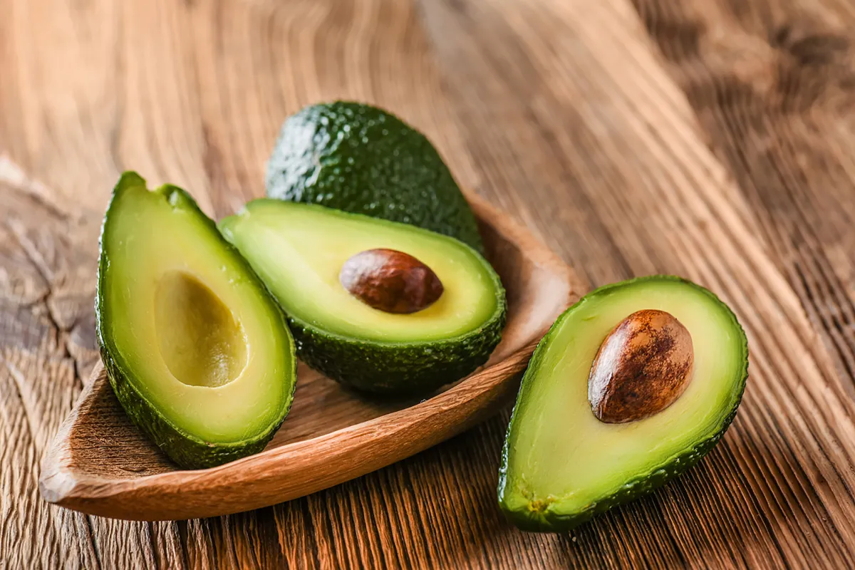 welche lebensmittel für gesunde haut strahlend avocado halbiert in kleiner holzschüssel