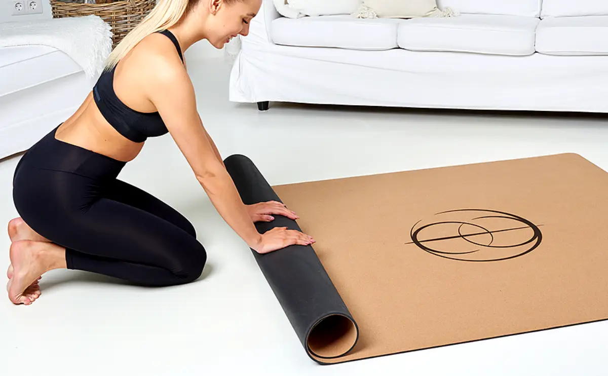 yogamatte kork reinigen frau in schwarzen leggings und bh rollt yogamatte aus kork